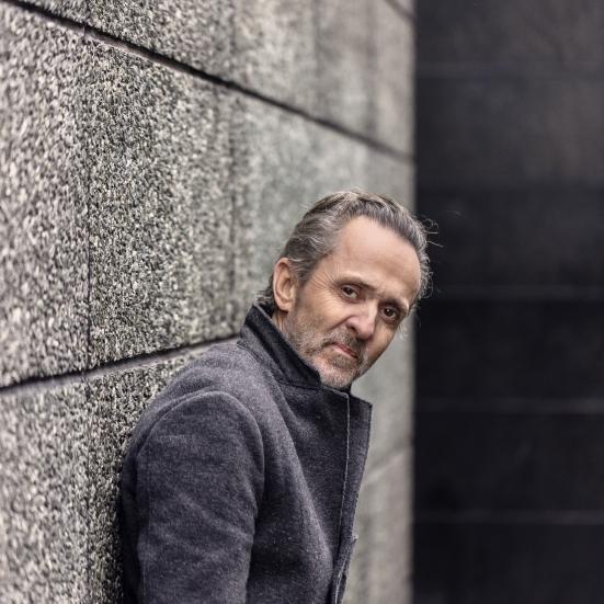 Forfatter Kim Fupz Aakeson står i en frakke og læner sig op ad en grå væg