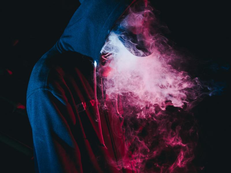 En person i hættetrøje puster damp ud fra en vape eller en puff bar