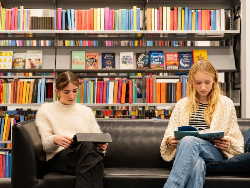 To unge sidder i en sofa og læser