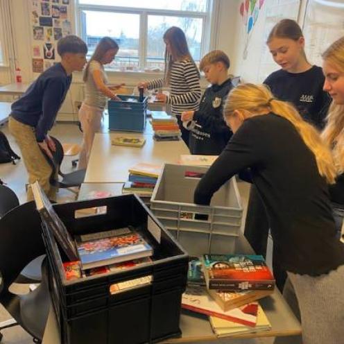 7 elever står rundt om borde fulde af bøger og transportkasser