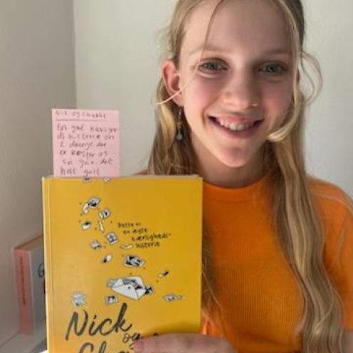Elev fra 7. klasse står med bogen "Nick og Charlie" i hænderne og kigger smilende ind i kameraet